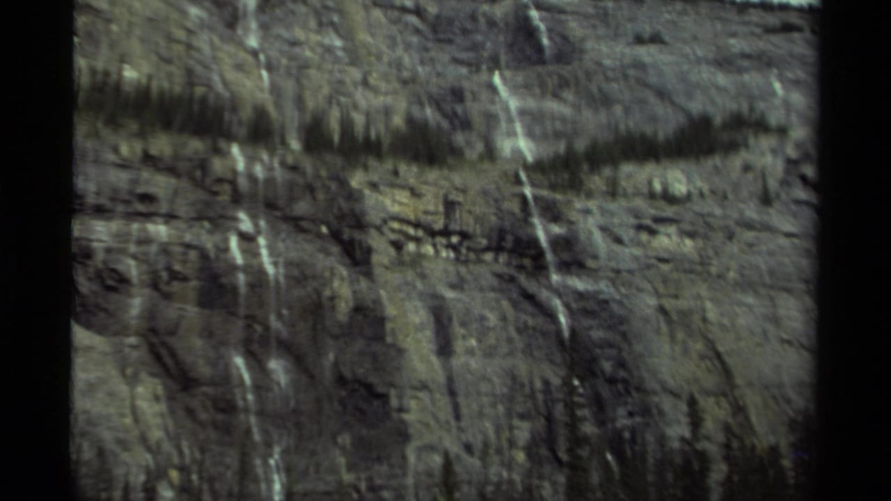 Distant cliff face with waterfalls and tree-lined upper ridge.