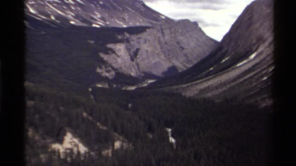 Canadian 8mm footage from 1979 appears to show evergreen forest beneath steep rock faces and a pale winding route or stream.