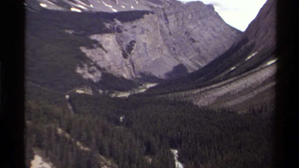 The final 1979 Canadian 8mm frame tightens on a forested valley, steep rock faces, and small snow patches in the mountains.
