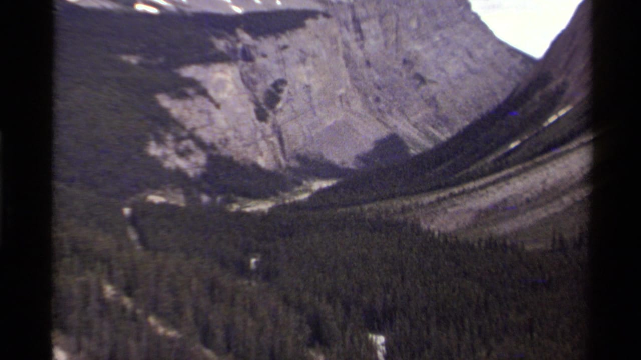 1979 8mm Canada footage showing evergreen forest across a valley beneath steep rocky mountain faces and small snow patches.