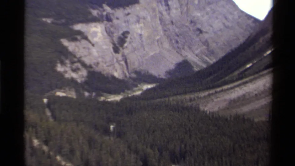 1979 8mm Canada footage showing a soft, grainy view across forested valley terrain toward steep mountain slopes.