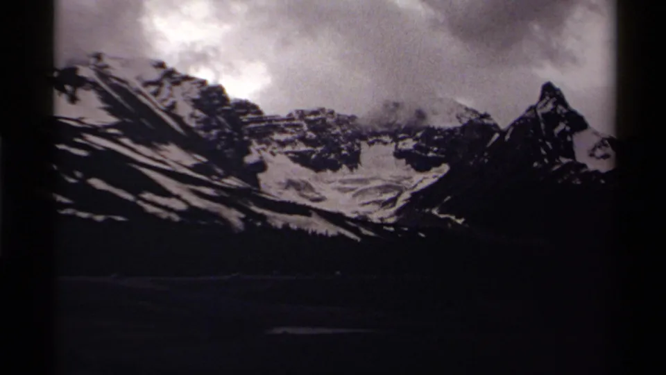 1979 8mm Canada frame showing a shadowed mountain range, snow patches, and dramatic cloud cover above the peaks.