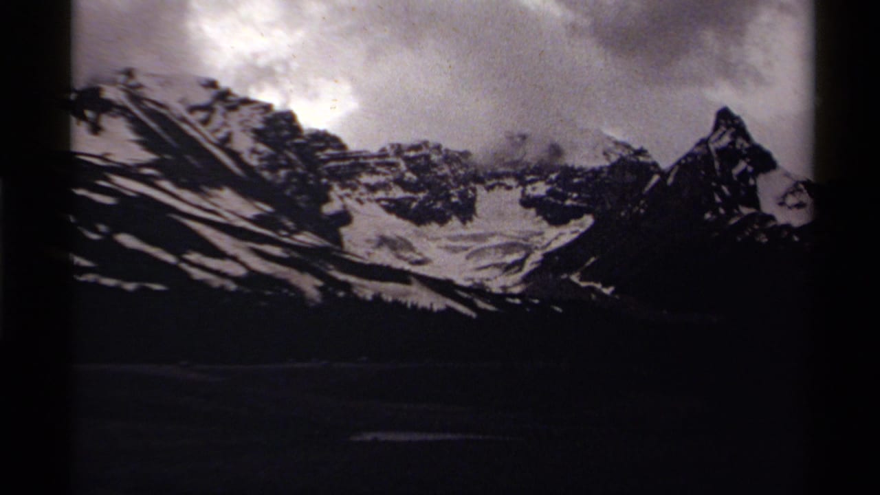 Snowy alpine ridges in Canada appear under heavy cloud in soft 8mm home-movie footage.