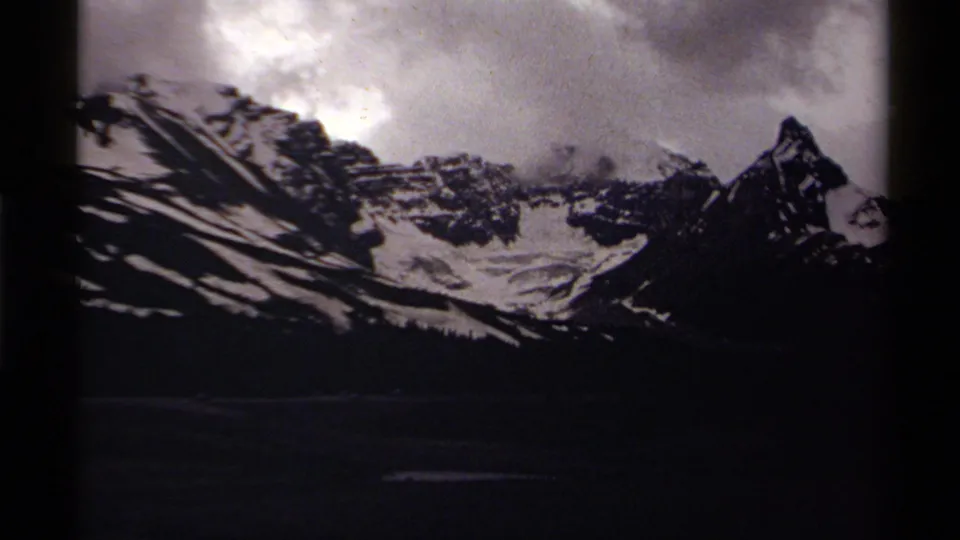 Snowy alpine ridges in Canada appear under heavy cloud in soft 8mm home-movie footage.