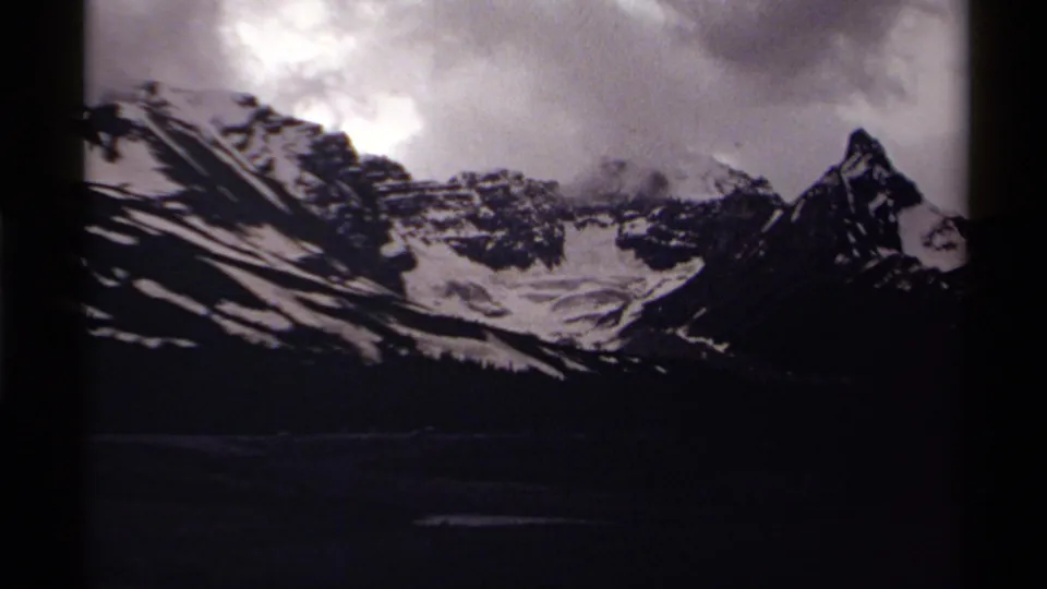 A snow-covered mountain range fills the frame, with clouds and dark 8mm frame edges visible.