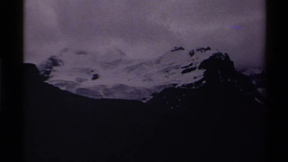 Home-movie view of a snow-capped mountain in Jasper National Park, framed by dark 8mm gate edges and low clouds.
