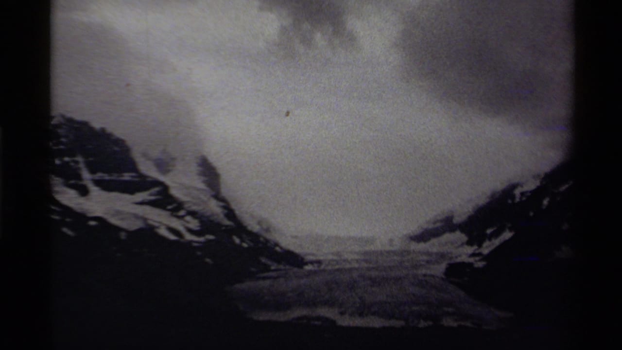 Snowy mountain valley beneath heavy clouds with dark slopes on both sides.