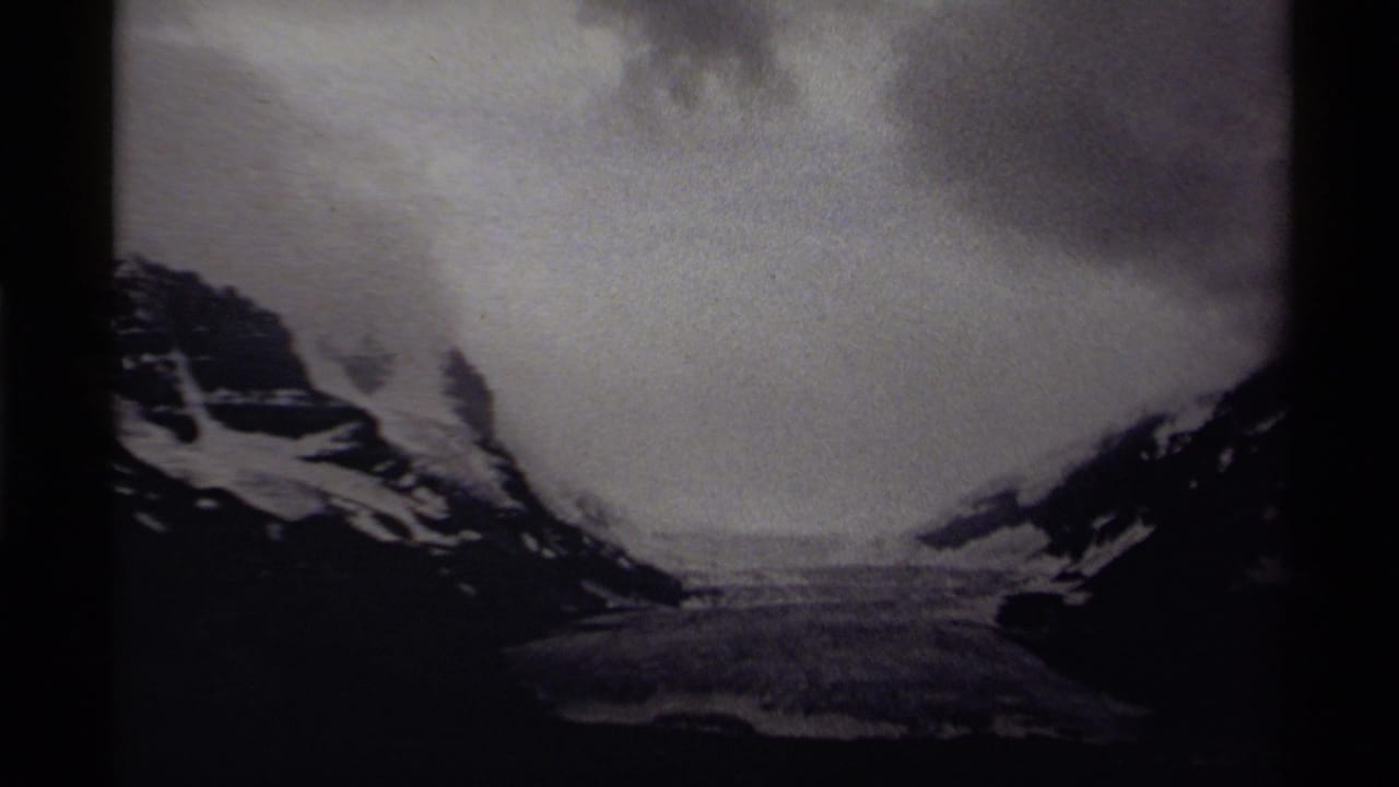 1979 Canadian 8mm frame with a snowy valley or frozen basin between mountains, filmed in soft black-and-white exposure.