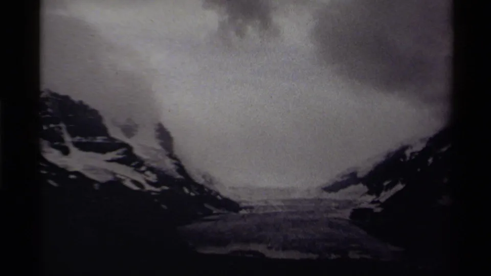 1979 Canadian 8mm frame with a snowy valley or frozen basin between mountains, filmed in soft black-and-white exposure.