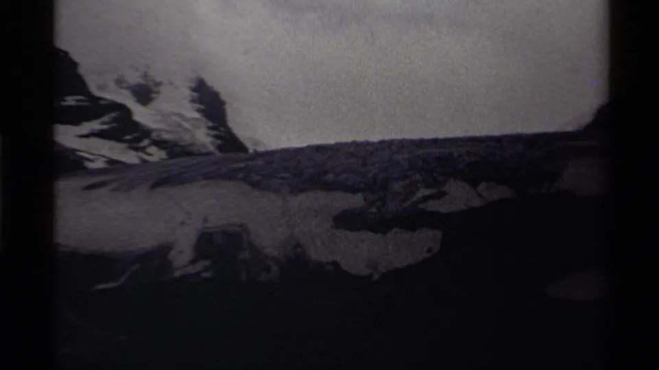 1979 Canadian 8mm frame showing a snow-covered mountain edge above a dark valley foreground in grainy monochrome.