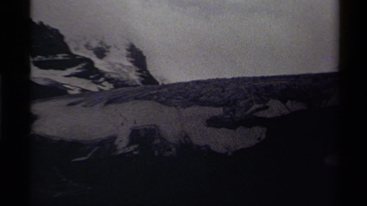 1979 Canadian 8mm frame showing dark rock faces, snowfields, and a distant mountain ridge under cloud cover.