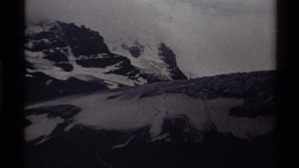 Black-and-white 8mm frame from Canada in 1979 showing a snow-covered mountain face, exposed rock, and overcast light.