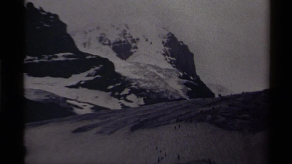 1979 Canada 8mm frame showing snow-covered peaks, dark rock faces, and small people moving across a broad icy foreground.