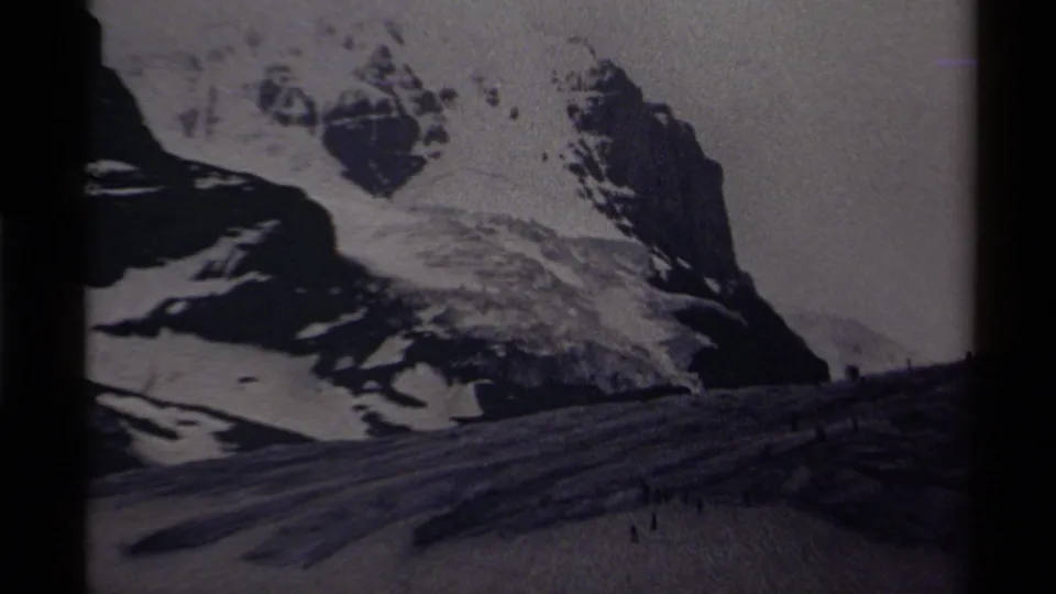 Distant 8mm view of a Canadian alpine snowfield with small figures under rugged, snow-covered peaks.