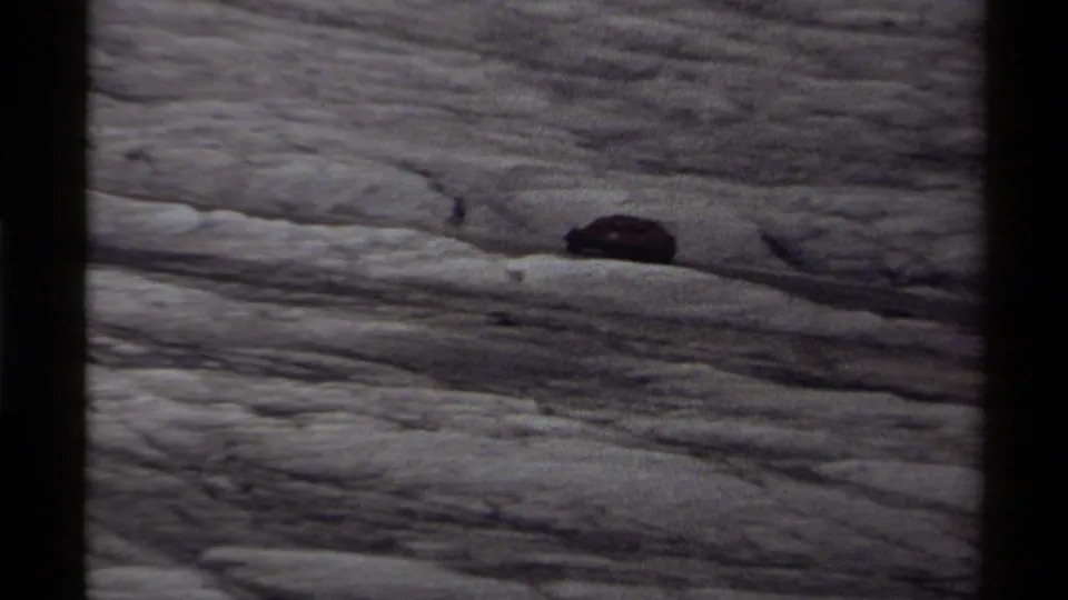 Distant 1979 Canada 8mm view of a dark vehicle on a rippled snowfield or glacier surface.