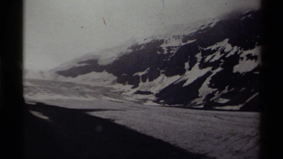1979 Canadian 8mm frame showing a snowy mountain valley, pale cloud cover, and a dark foreground edge.