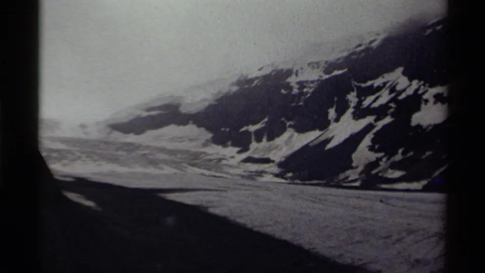 1979 Canadian 8mm frame showing a snowy mountain slope, broad icy terrain, overcast sky, and dark film gate edges.