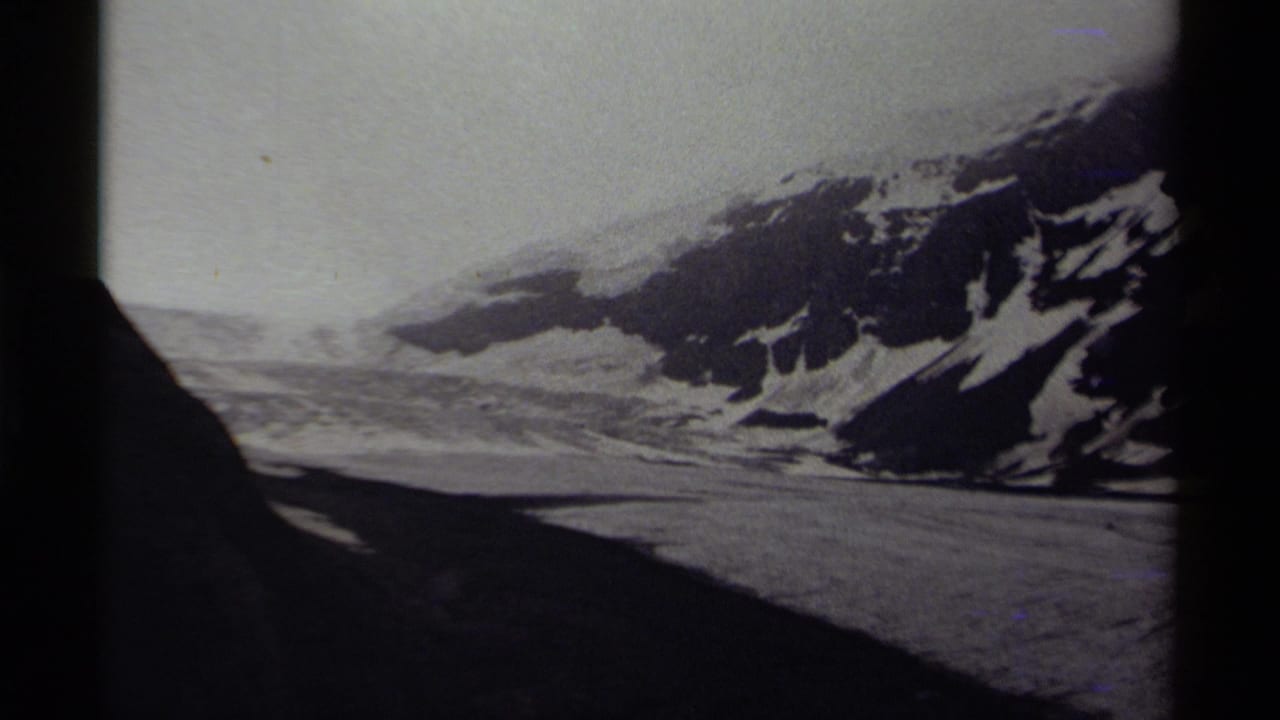 Black-and-white 8mm view of a Canadian snow-covered mountain landscape with a dark foreground shadow and hazy sky.