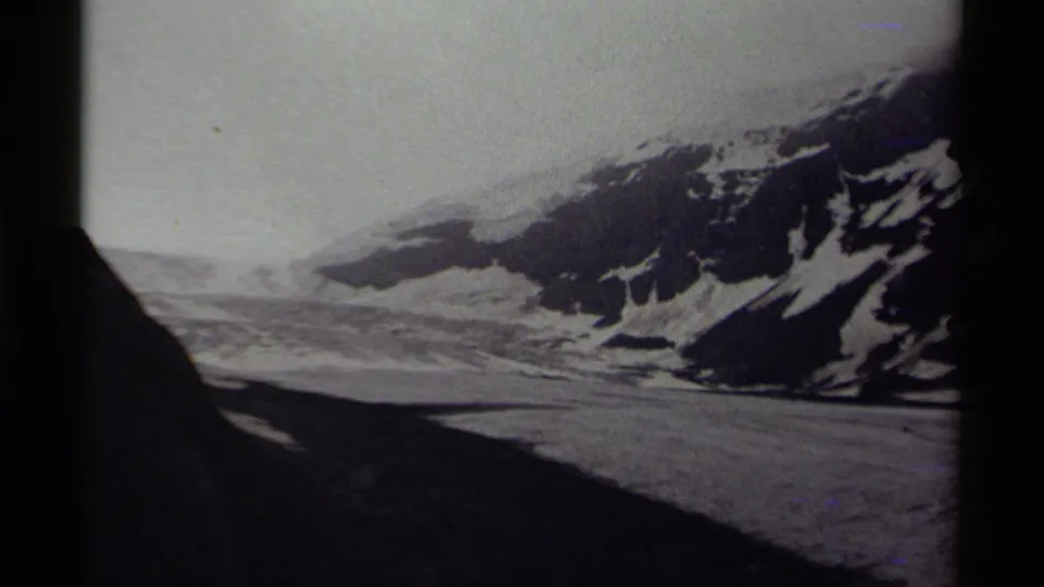 Black-and-white 8mm view of a Canadian snow-covered mountain landscape with a dark foreground shadow and hazy sky.