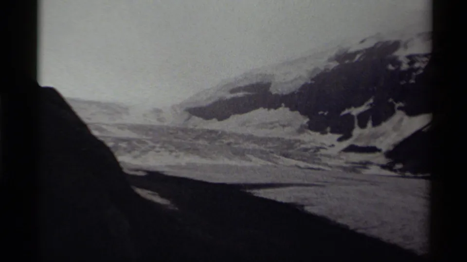 Black-and-white Canadian 8mm frame with a distant snowfield, rugged dark ridge, and shadowed foreground near the film edge.