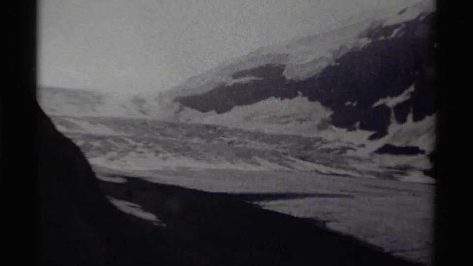 1979 Canada 8mm frame showing a distant snowy mountain landscape, dark rock forms, and pale winter sky.