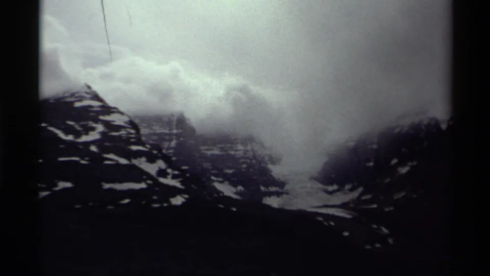 1979 Canada 8mm frame showing snow-streaked mountain slopes partly obscured by low clouds and soft archival grain.