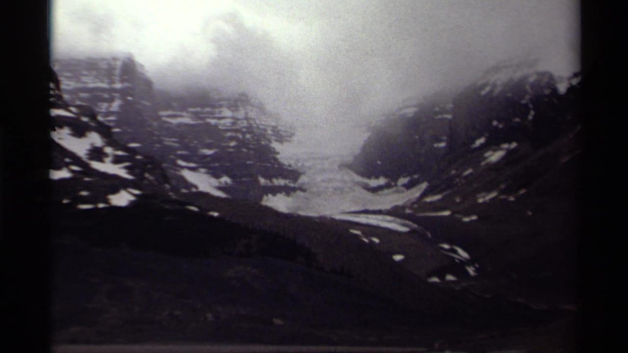 Canadian mountain landscape on 8mm film, with a glacier centered between rocky slopes and low cloud cover.