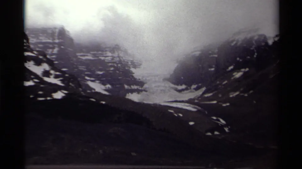 Canadian mountain landscape on 8mm film, with a glacier centered between rocky slopes and low cloud cover.
