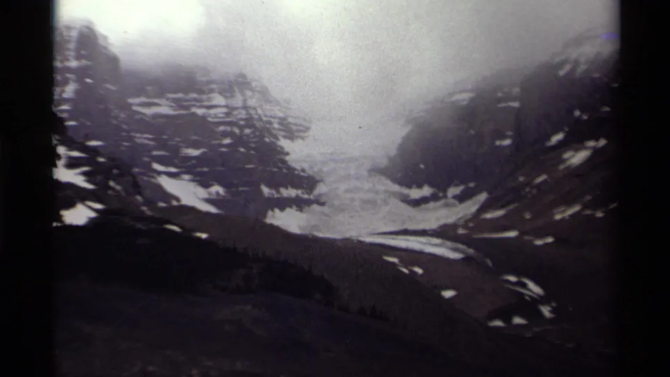 Closer 1979 8mm view of a glacier descending through a Canadian mountain valley beneath misty cloud.