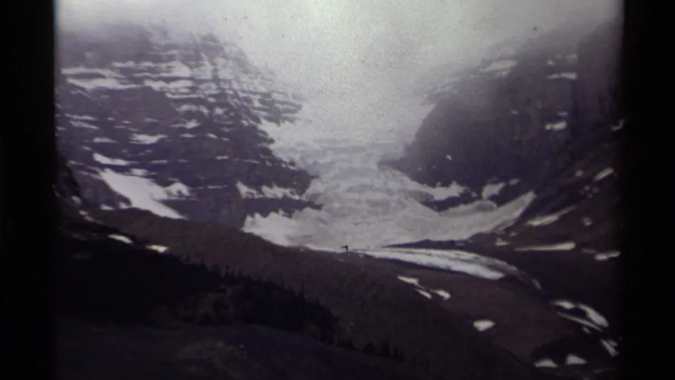Soft 8mm frame of a Canadian glacier valley, with dark mountain sides, snow patches, and a clouded sky.