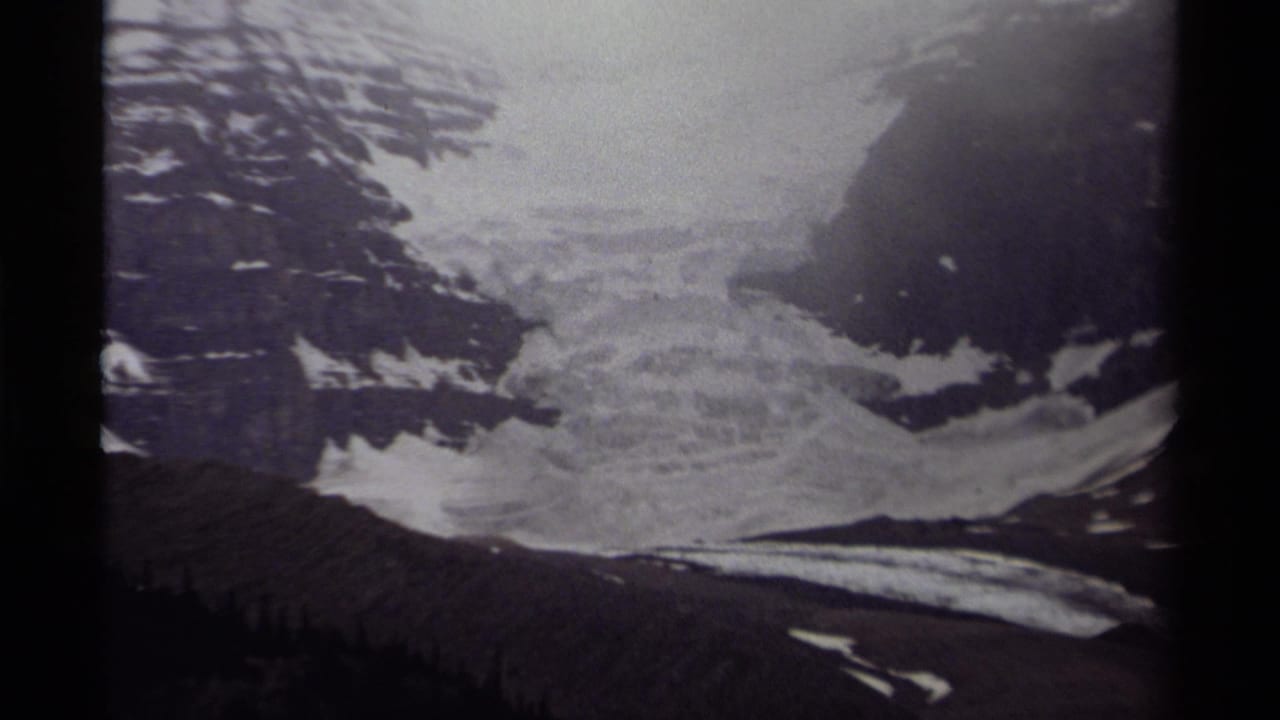 Grainy 1979 Canadian 8mm frame showing a broad glacier below steep alpine rock faces.