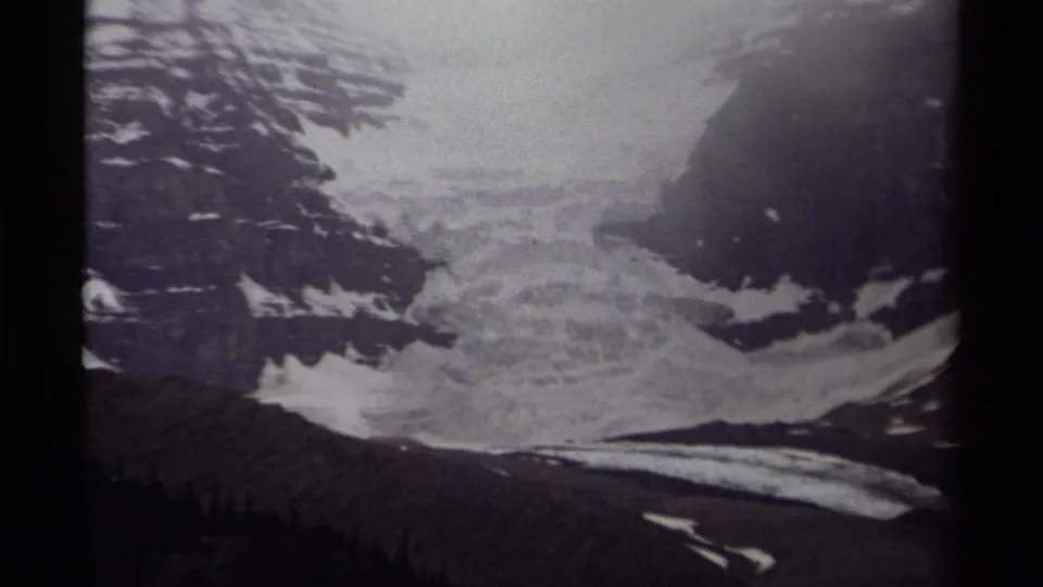 Grainy 1979 Canadian 8mm frame showing a broad glacier below steep alpine rock faces.
