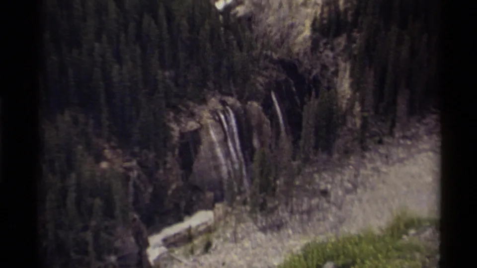 1979 Canadian 8mm view of a waterfall cutting through dense evergreens and pale rock.