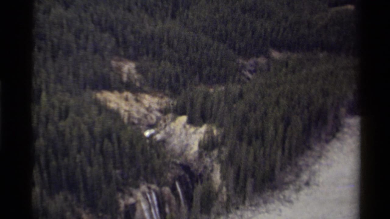 1979 Canadian 8mm frame showing an overhead view of dense evergreens, rocky terrain, a waterfall, and river water through the valley.