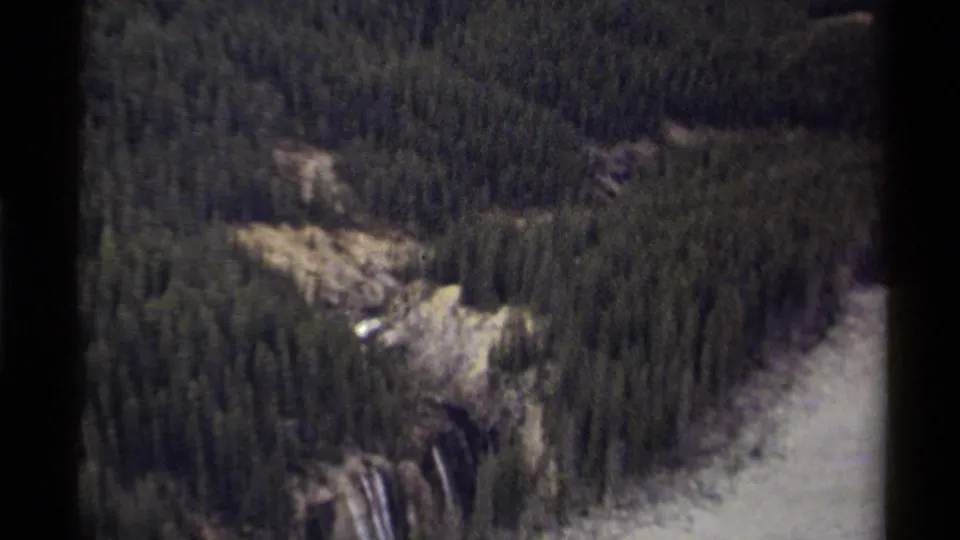 1979 Canadian 8mm frame showing an overhead view of dense evergreens, rocky terrain, a waterfall, and river water through the valley.