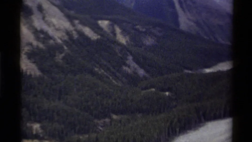 1979 Canadian 8mm aerial view over a darker mountain valley, showing forested slopes, ridgelines, and pale river water below.