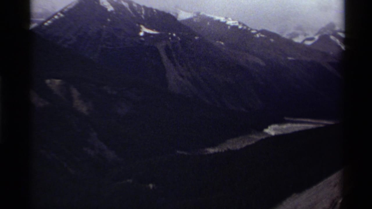 1979 Canada 8mm view of rugged mountain slopes with snow patches and a bright water or ice feature below.