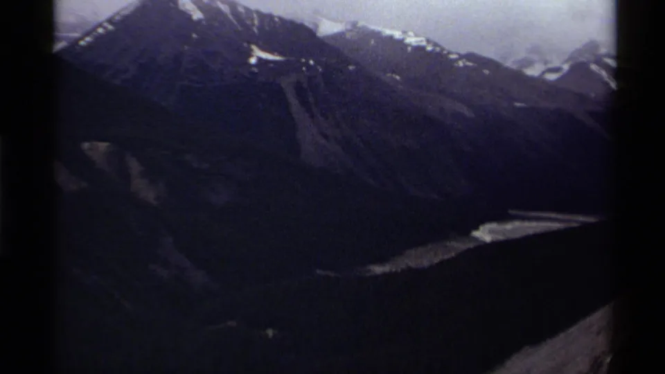 1979 Canada 8mm view of rugged mountain slopes with snow patches and a bright water or ice feature below.