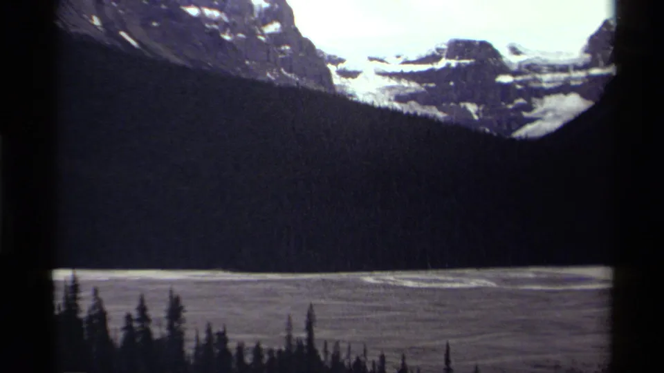 1979 Canada 8mm view across a forested mountain valley toward snowfields and bright high ridges.