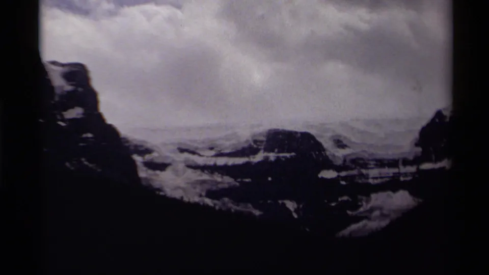 1979 8mm Canadian wilderness view with distant snow-streaked peaks, heavy clouds, and dark mountain silhouettes at the frame edges.