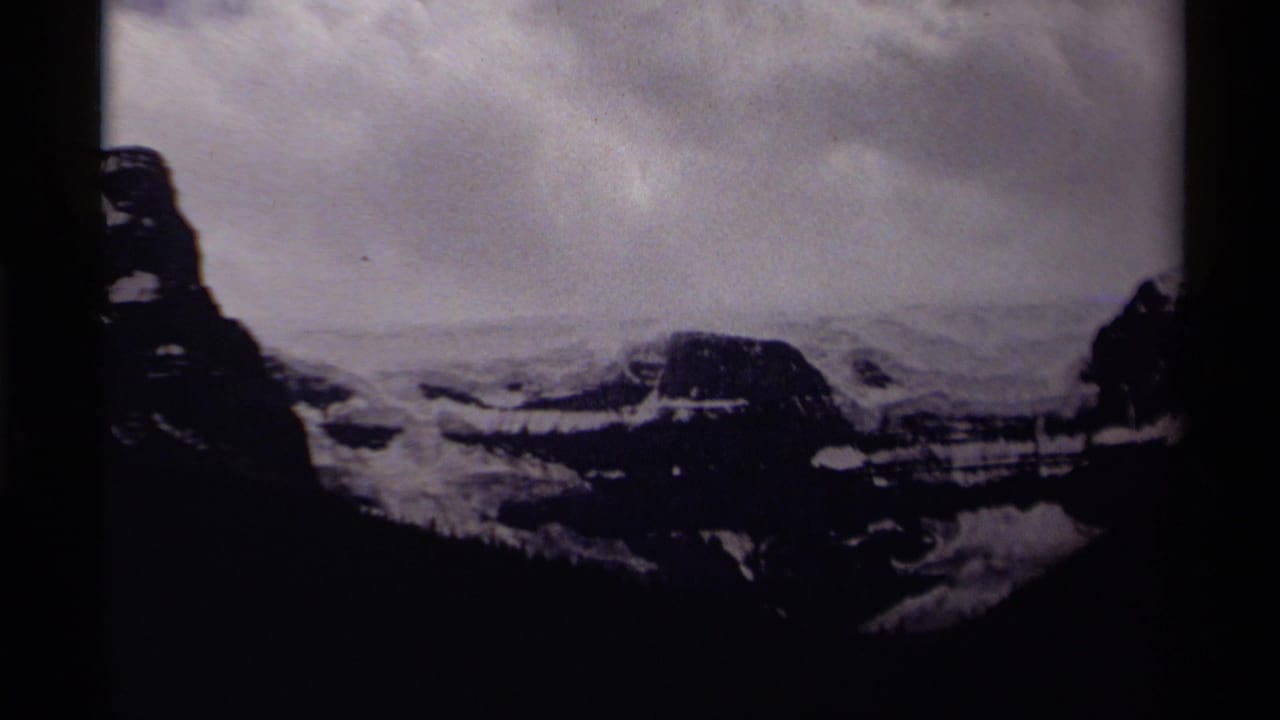 Dark snow-covered mountain landscape under an overcast sky within visible film-frame borders.