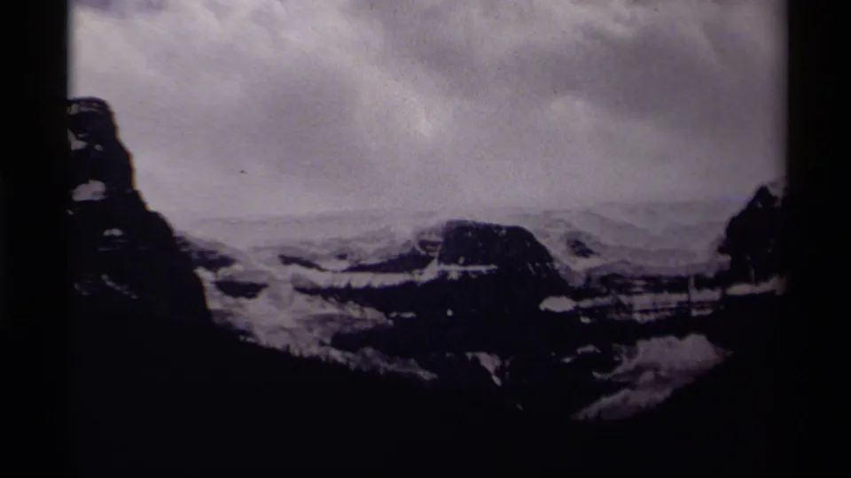 1979 Canada 8mm frame showing a dark, high-contrast mountain scene with snow patches, rocky slopes, cloudy sky, and film-frame edges.