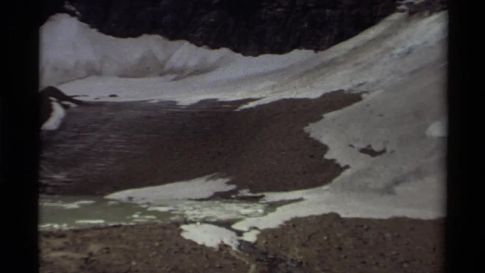 1979 Canada 8mm frame showing snow-covered ground, exposed gravel, icy runoff channels, and a dark ridge line above.