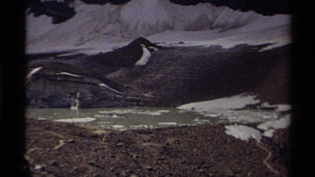 Alpine lake with scattered ice below dark rock and snow-covered slopes.