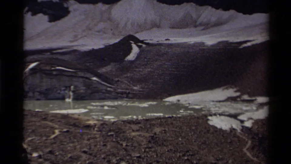 1979 Canada 8mm view of a murky alpine lake with ice fragments, exposed rock, and lingering mountain snow.