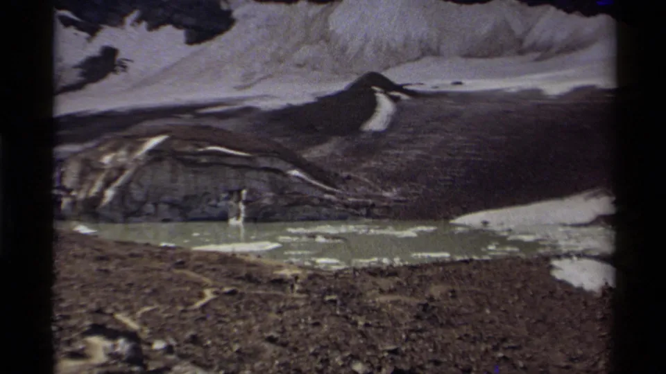 1979 Canada home-movie frame with rocky terrain, a pale lake with ice, and snow melting along the mountain basin.