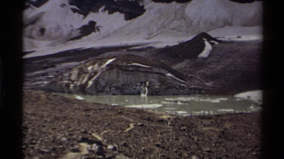 1979 Canada 8mm frame showing a rugged mountain basin, pale lake water, melting snow, and exposed rocky ground.