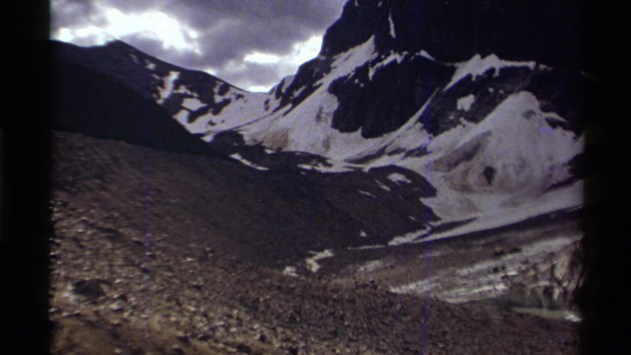 Snow-capped mountains under a cloudy sky with rocky valley terrain below.