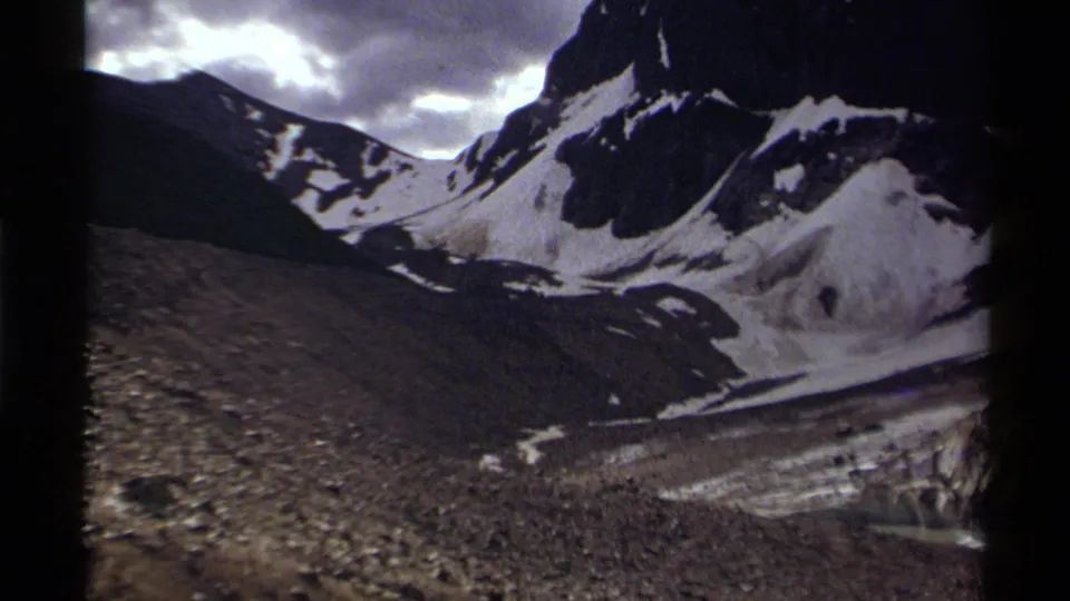 1979 Canadian 8mm view of a rugged snow-covered mountain ridge with dark slopes and bright cloud breaks overhead.