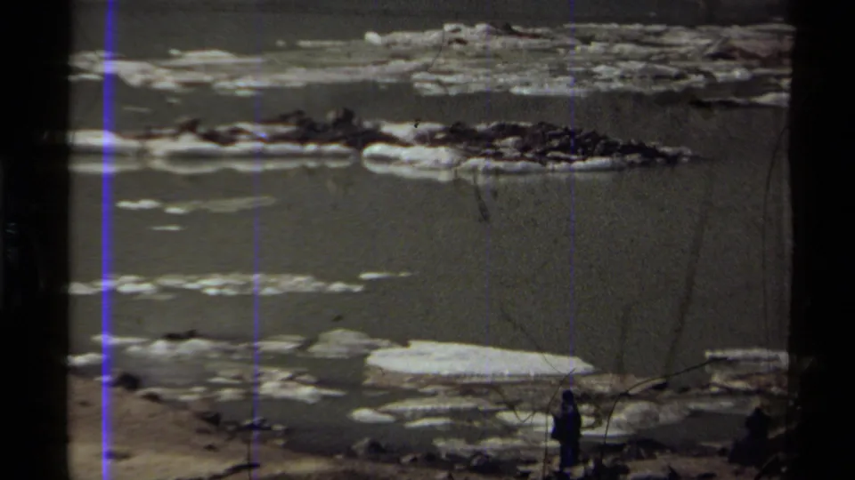 1979 Canadian 8mm frame showing floating ice, a rocky shoreline, and distant people partly silhouetted near the lower right and lower center.